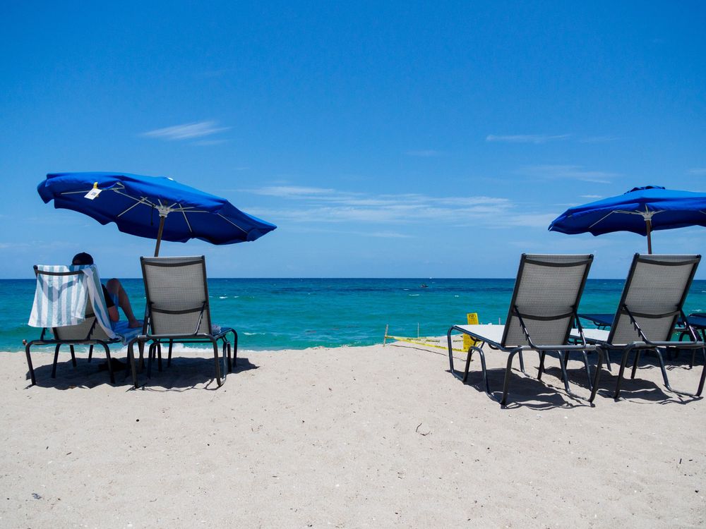 Blue beach umbrellas and lounge chairs on a white sandy beach with turquoise ocean water.