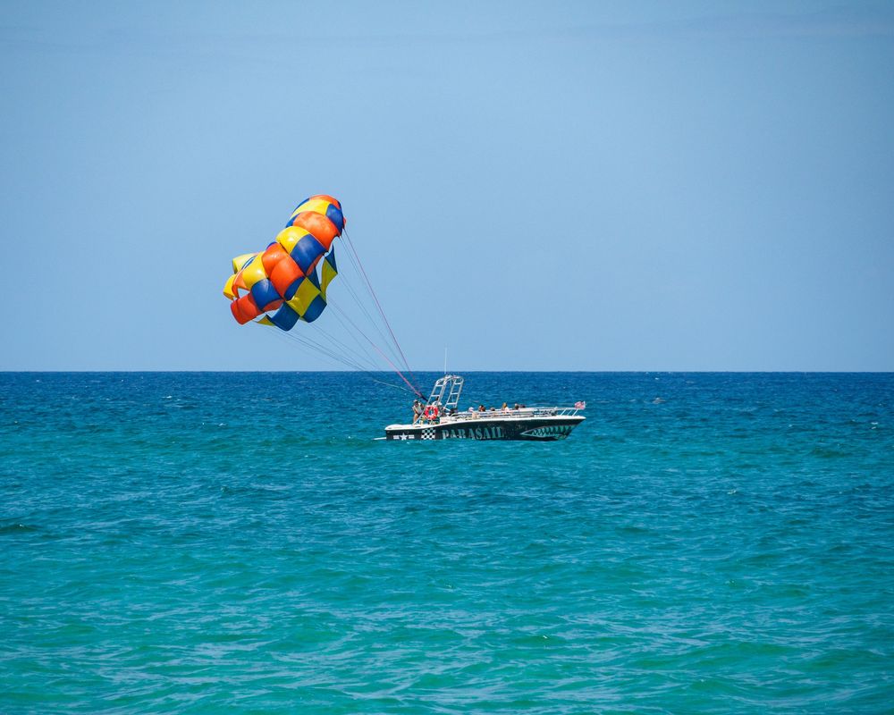Colorful parasail parachute attached to a boat floating on bright turquoise ocean water.