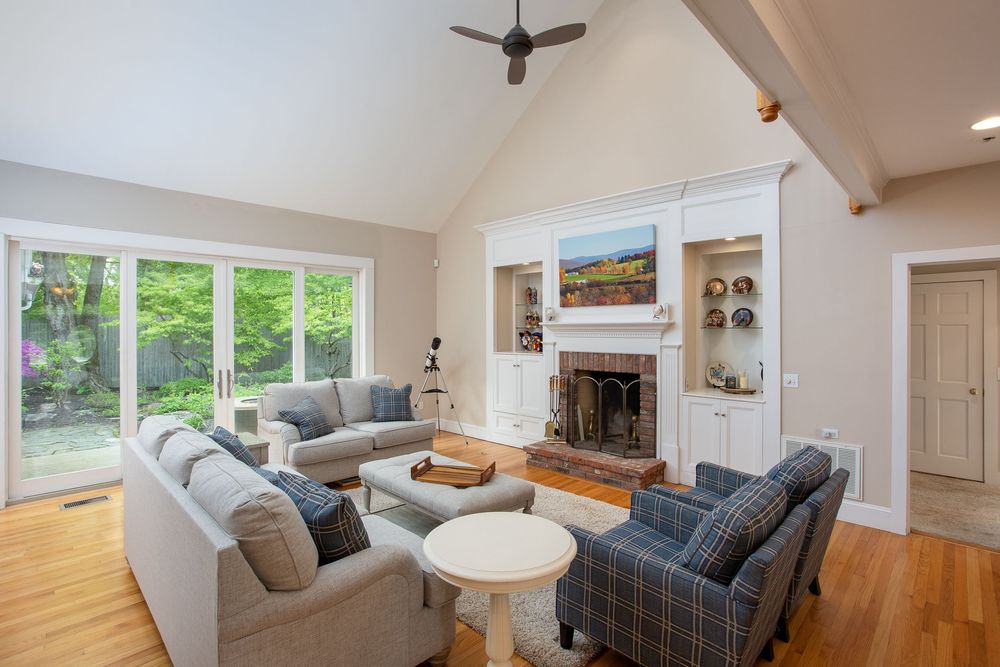 Bright vaulted living room with built-in shelving, stone fireplace, large windows, and hardwood floors.
