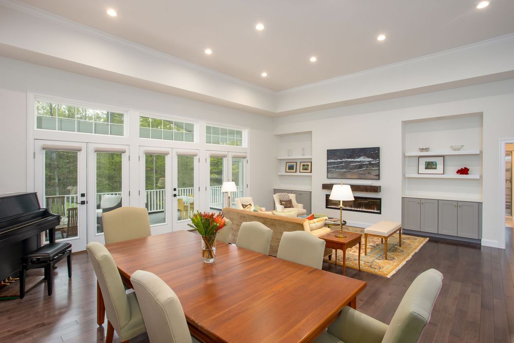 Elegant open-plan living and dining room with hardwood floors, French doors, built-in shelves, and a modern fireplace.