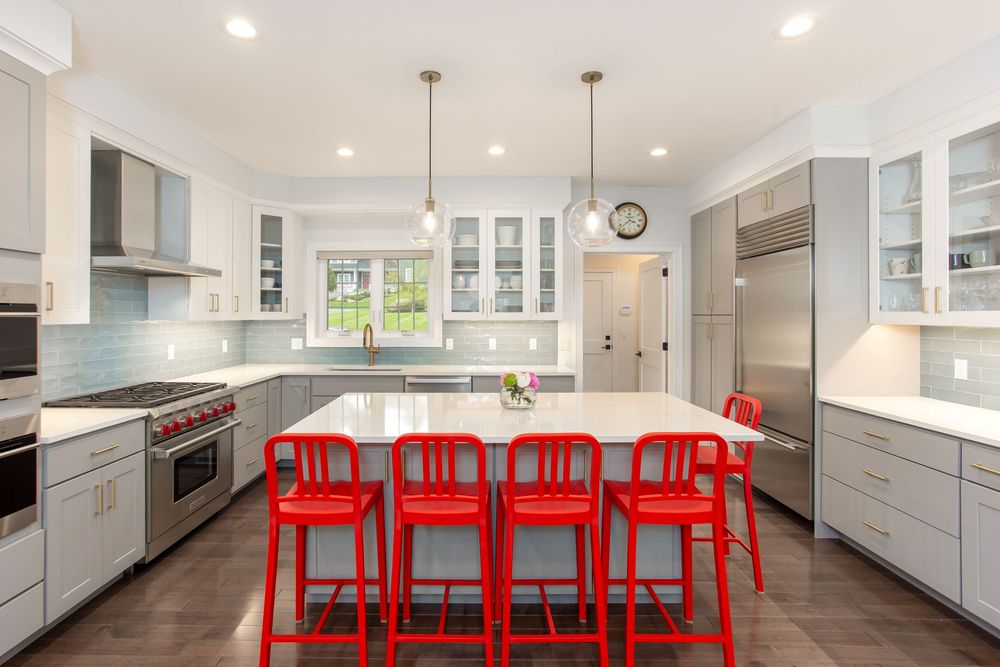 Contemporary kitchen with gray cabinets, white island, red bar stools, pendant lights, and stainless appliances.