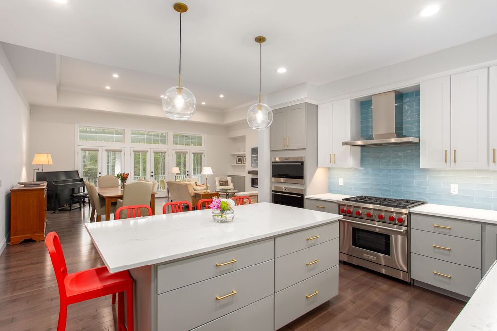 Modern kitchen with gray island, white quartz countertops, globe pendant lights, blue backsplash, and stainless steel range.