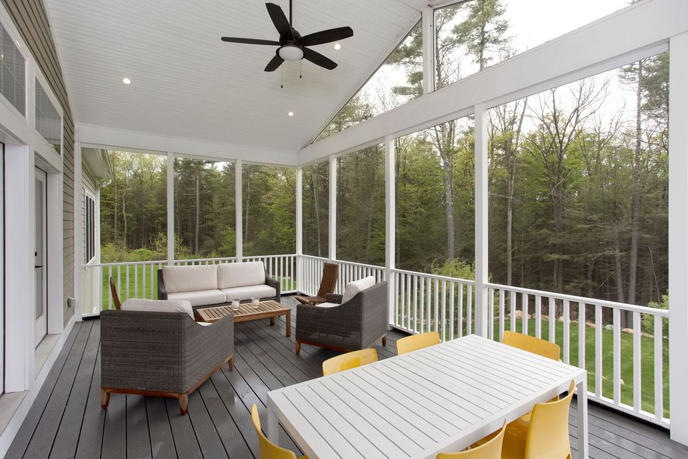 Screened porch with ceiling fan, wicker furniture, dining table, and serene wooded views.