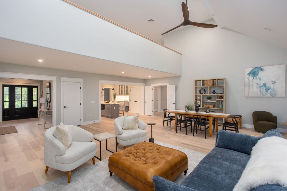 Spacious open-concept living room with vaulted ceilings, tufted ottoman, and view into dining and kitchen areas.