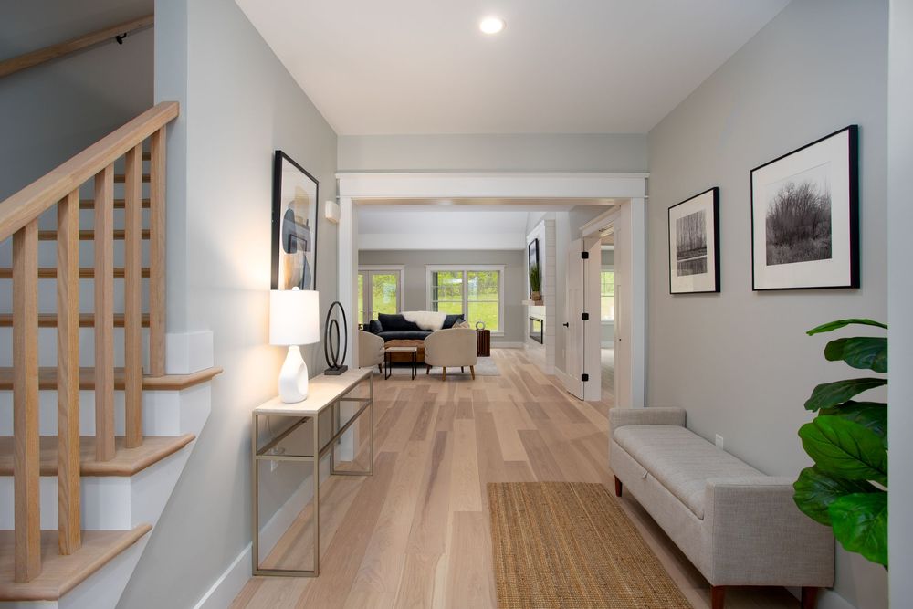 Bright entryway with light hardwood floors, staircase, console table, framed artwork, and views to living area.