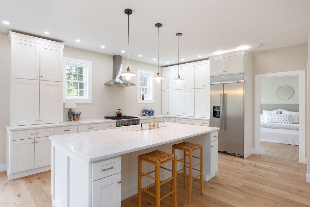White kitchen with quartz island, bar stools, stainless steel appliances, and light hardwood floors.