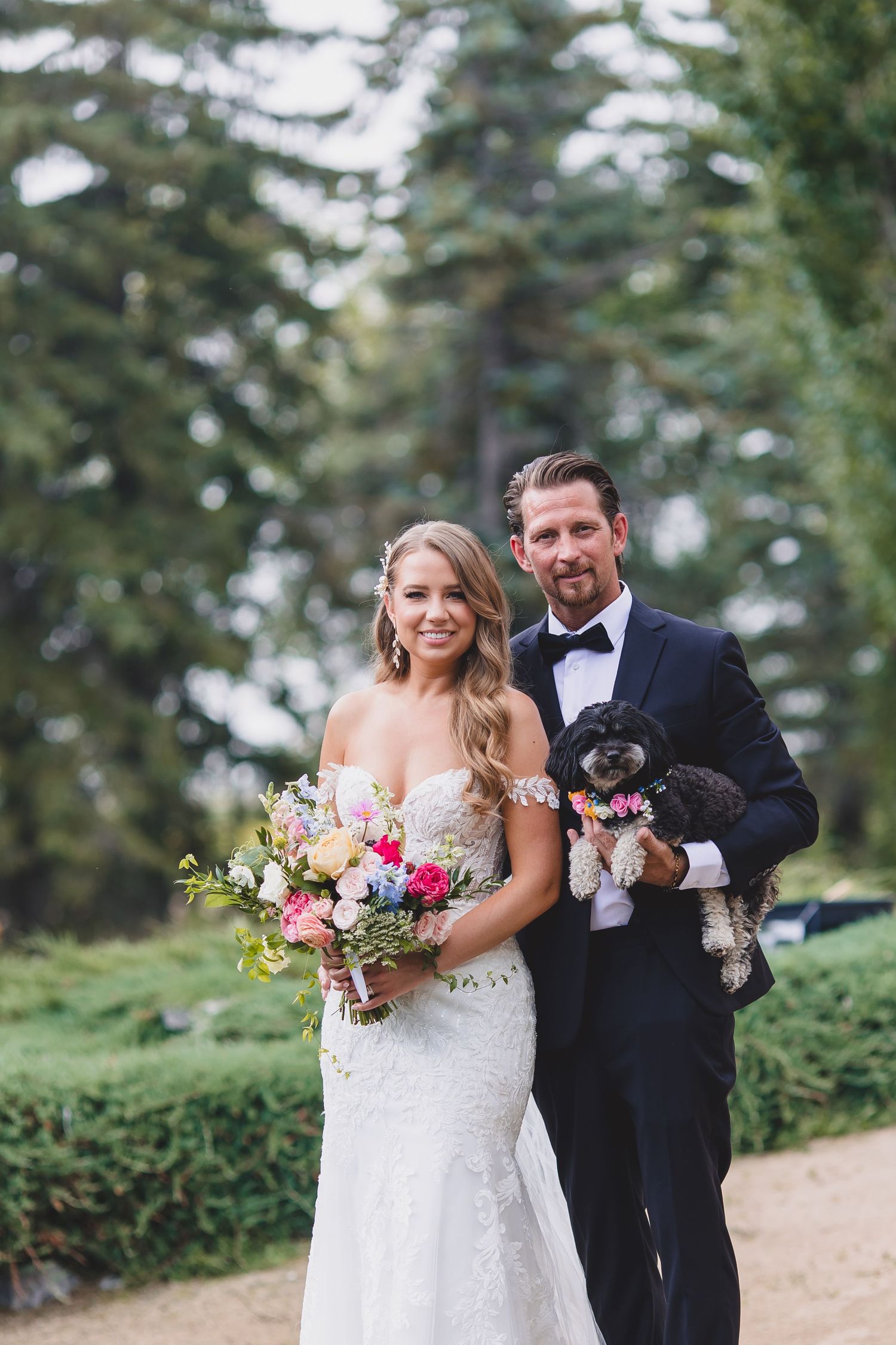 Two people in white wedding dresses embrace while smiling at the camera in a bright room with a rustic door. Hawthorne Estates
