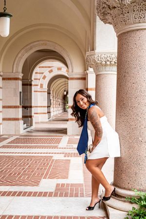 Woman in white dress and blue tie posing in elegant arched corridor with ornate columns.