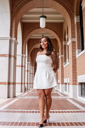 Woman in white strapless mini dress and heels posing under brick arched colonnade hallway.