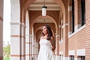 Woman in white strapless dress posing under brick arches of elegant building corridor with hanging pendant light.