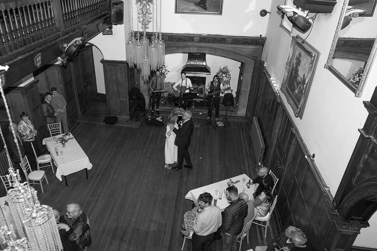 Black and white aerial view of a wedding reception in a historic hall with guests, dining tables, and a live band.