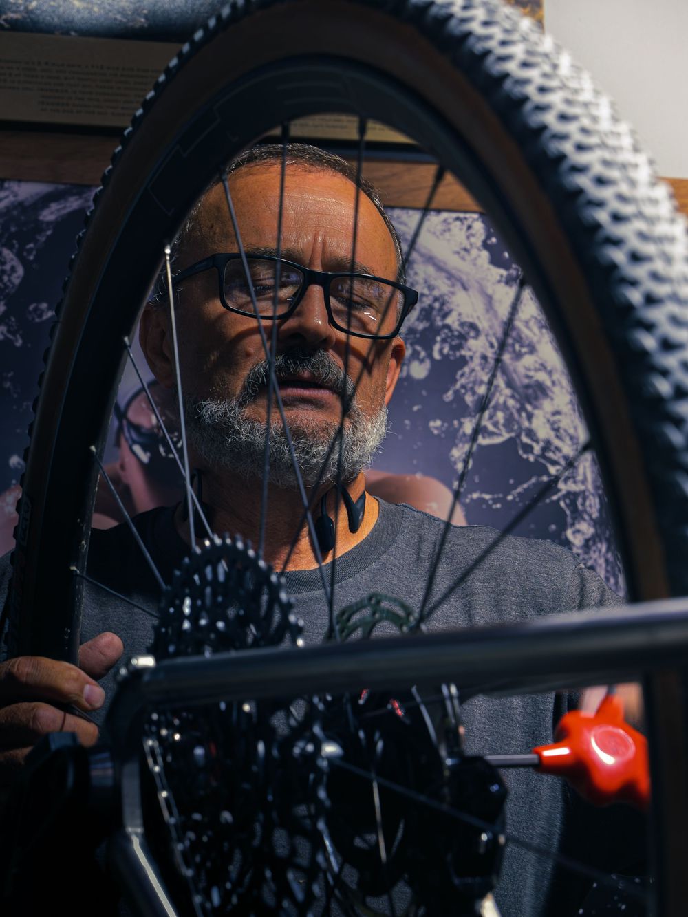 The owner of Velocity Multi Sport & Cycling focused on a mountain bike wheel, framed through the spokes in his Janesville shop.
