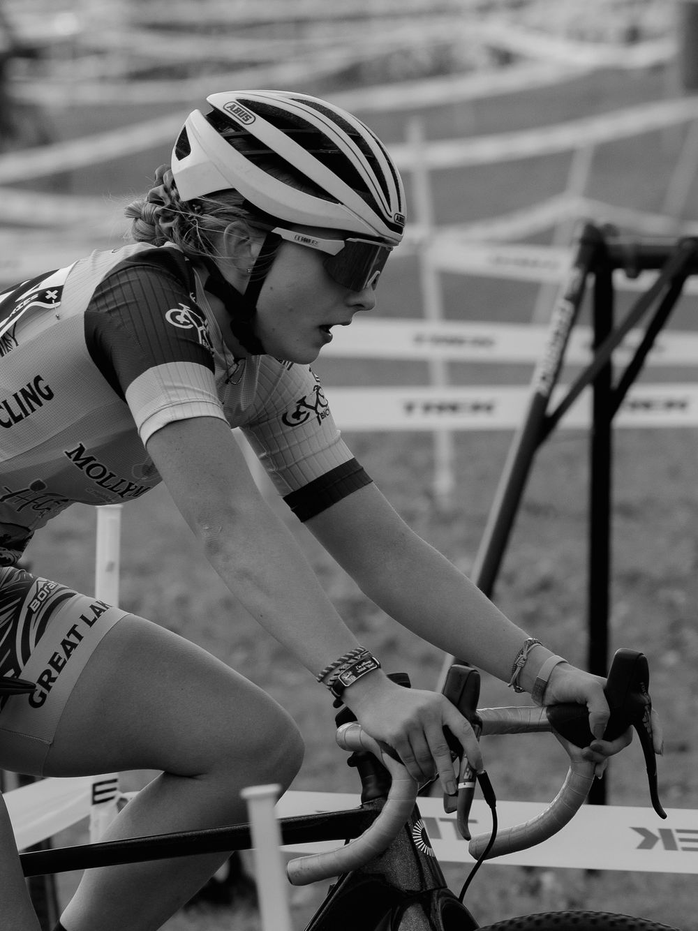Black-and-white profile of a cyclocross racer mid-effort on the course, hands on the drops, jaw set and eyes locked on the trail ahead.