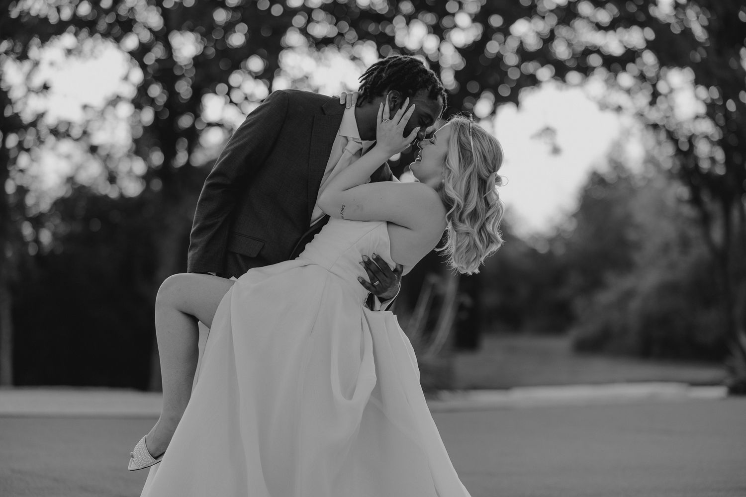 Black and white photo of a bride and groom sharing a romantic dip kiss outdoors on their wedding day.
