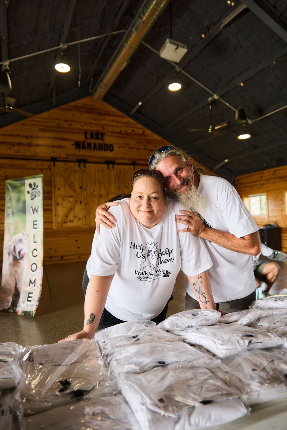 Two volunteers smile at a charity walk event table inside a wooden barn at Lake Wanahoo.