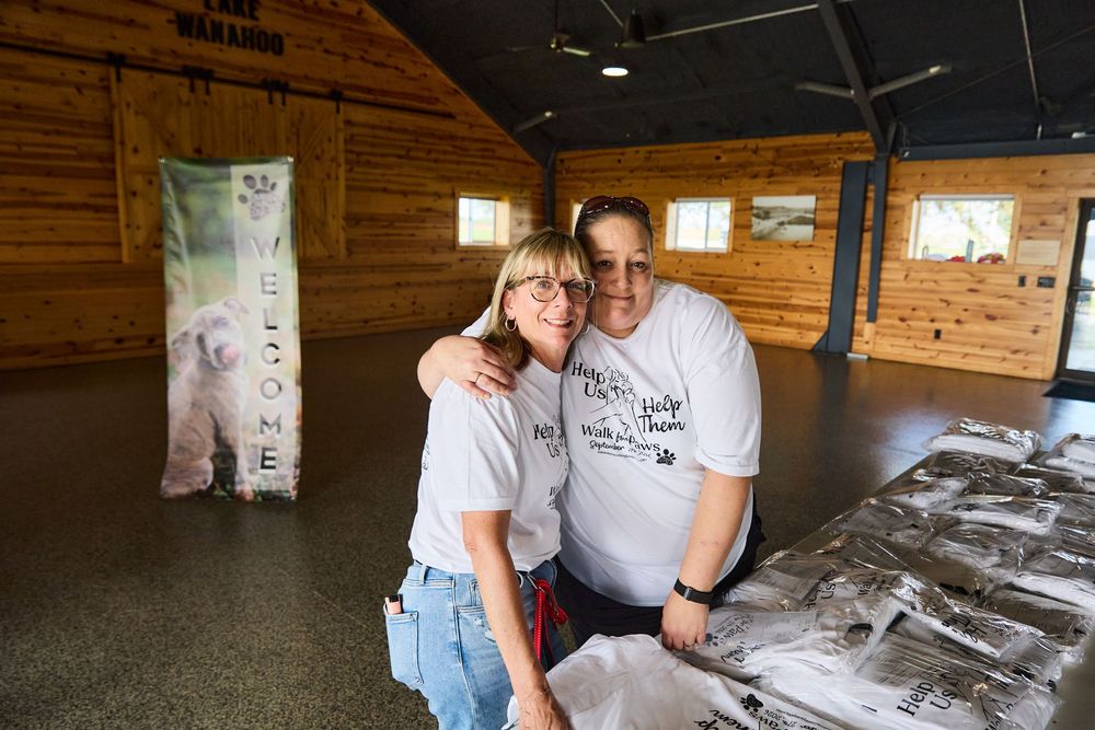 Two volunteers in matching white t-shirts smile together inside a rustic wooden barn venue during a charity event.