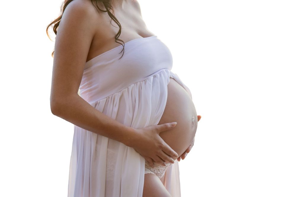 mother holding her pregnant belly wearing a sheer white open front dress