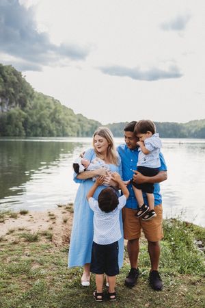 Family of four posing by a scenic river, parents holding young children, dressed in blue coordinated outfits.