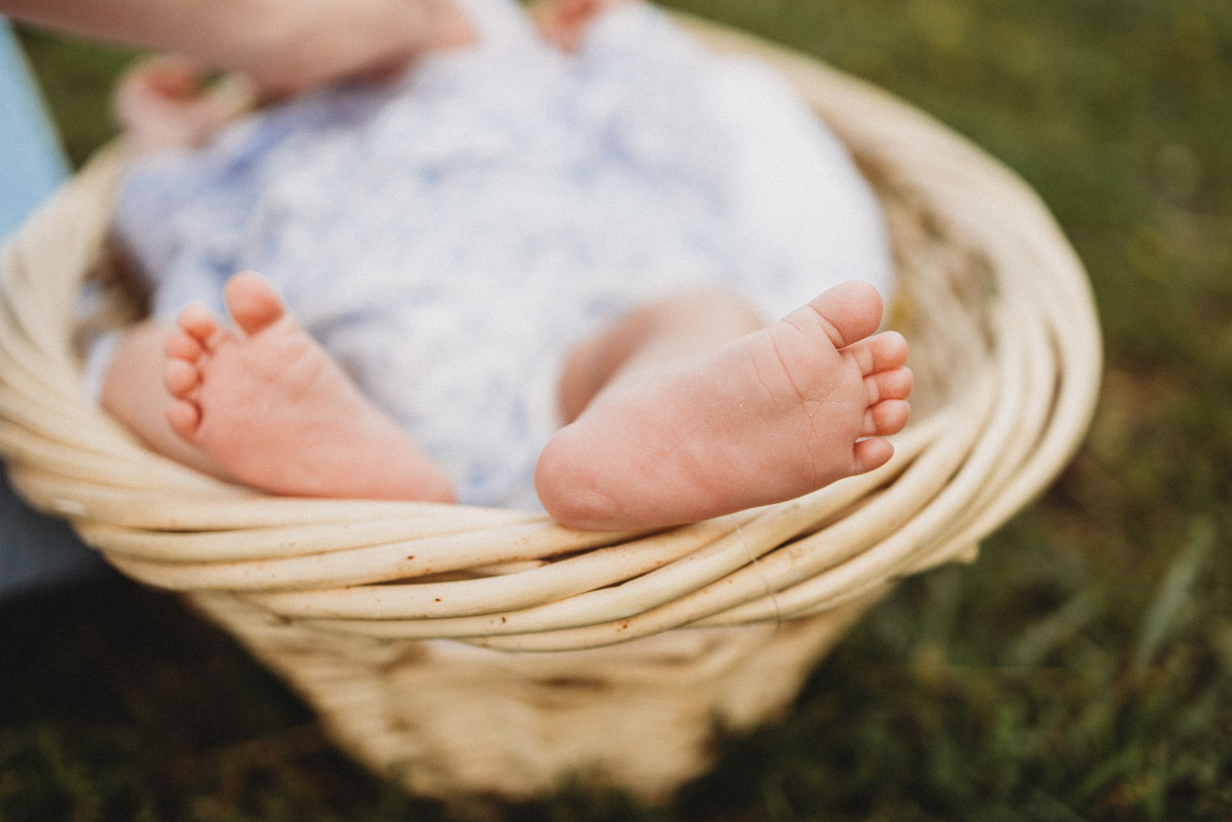 Close-up of tiny baby feet resting in a wicker basket on green grass outdoors.