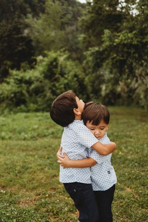 Two young brothers in matching shirts share a warm hug outdoors on a green grassy field at Melton Hill Park in Knoxville, TN