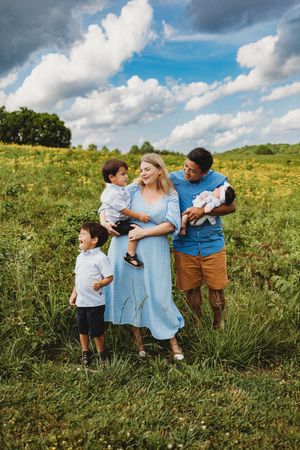 Happy interracial family with three children poses in a sunny wildflower meadow under a cloudy sky at Melton Hill Park in Knoxville, TN