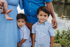 Two young boys in matching blue shirts pose together outdoors during a family photo session near a pond.