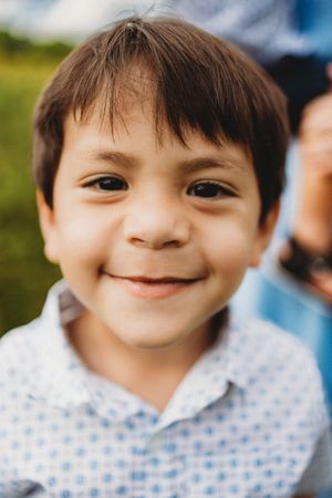 Close-up portrait of smiling young boy with dark hair wearing a blue patterned shirt outdoors at Melton Hill Park in Knoxville, TN