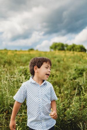 Happy young boy in blue patterned shirt laughing in a green meadow under dramatic cloudy sky at Melton Hill Park in Knoxville, TN
