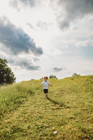 A young child runs down a grassy hill path under dramatic cloudy skies in an open field at Melton Hill Park in Knoxville, TN