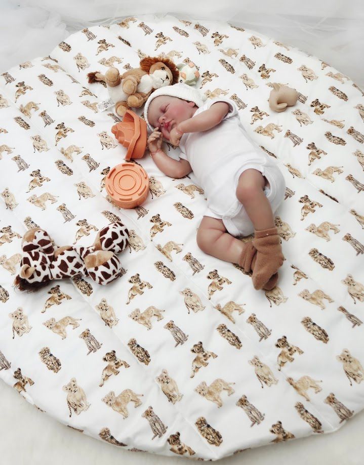 Sleeping newborn baby on a round white safari animal print play mat surrounded by soft toys and teethers.
