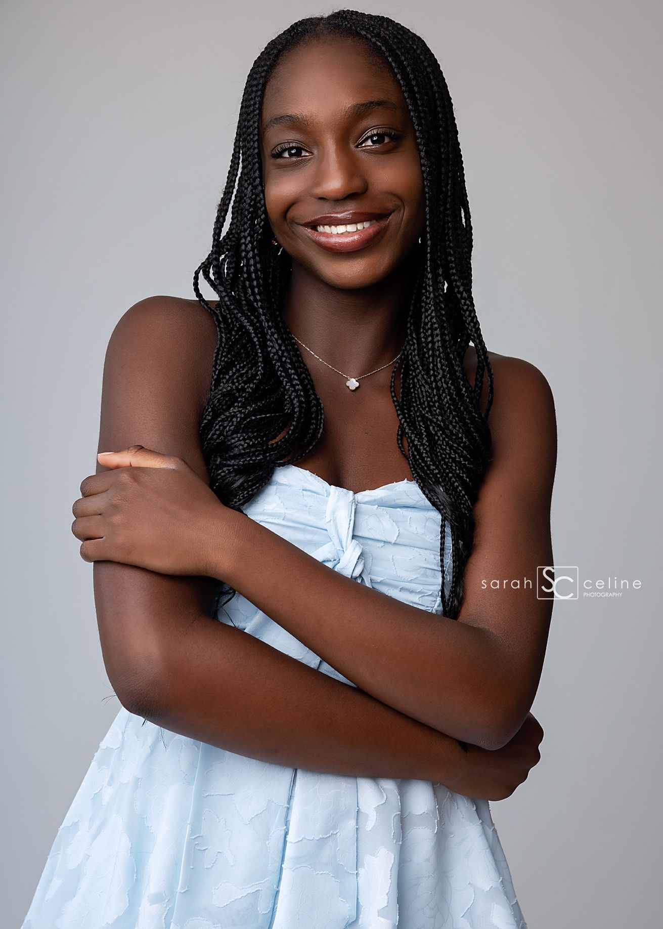 Young woman with braids in a light blue strapless dress smiling confidently in a professional studio portrait.