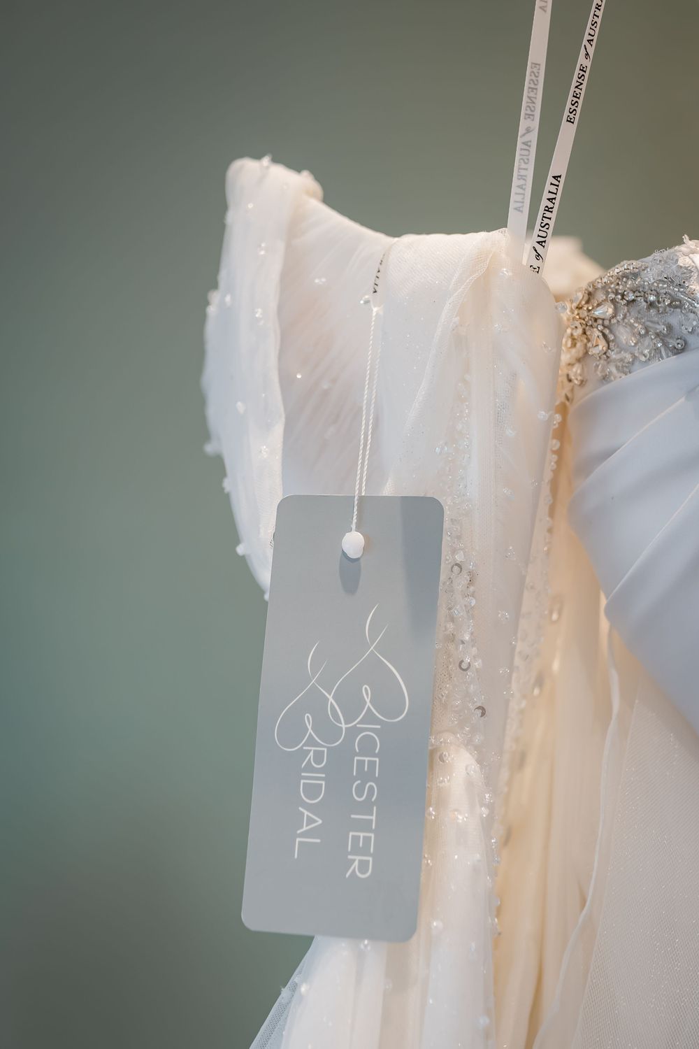 White beaded wedding dress on hanger with Bicester Bridal tag, featuring delicate embellishments and flowing fabric.