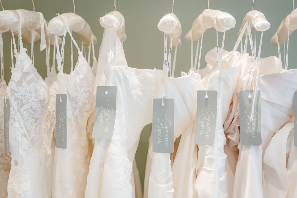 Row of elegant white wedding dresses hanging on hangers with grey tags in a bridal boutique.