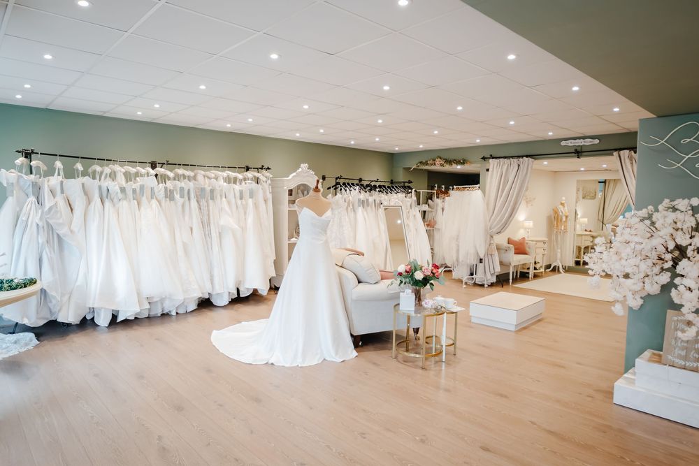Elegant bridal boutique showroom displaying rows of white wedding dresses on racks with hardwood floors and soft lighting.