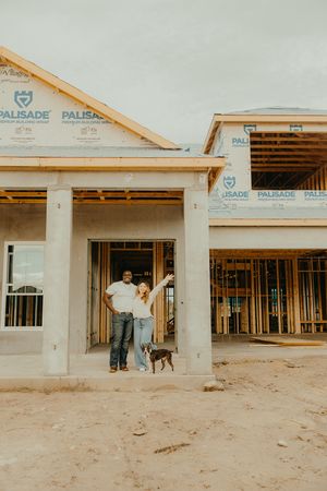 Couple and dog posing in front of their new home under construction with Palisade wrap visible on framing.