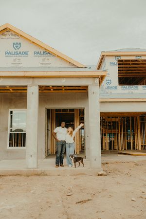 Couple and dog pose in front of their new home under construction with Palisade wrap visible on framing.