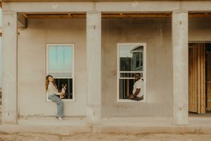 Couple sitting in separate windows of a home under construction with stucco exterior walls.