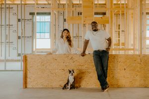 Couple and dog pose in unfinished home construction site with wood framing and OSB panels.