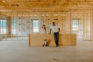 Couple and dog standing in unfinished new home construction with wood framing and OSB panels.