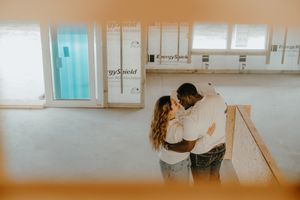 Interracial couple embracing romantically inside their new construction home with exposed wood framing.