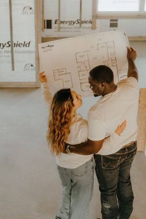 Couple reviewing house blueprints together inside a home under construction.