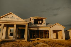 Couple stands in the second-floor frame of their new home under construction at golden hour.