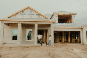 Two people stand in front of a new home under construction with exposed framing and Palisade building wrap visible.