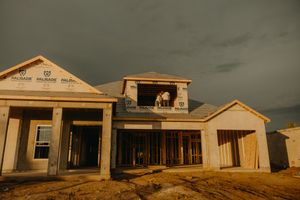 New construction home exterior at dusk with dramatic stormy sky and unfinished stucco walls.