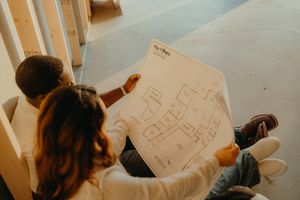 Couple reviewing house blueprints together while sitting on stairs inside their new construction home.