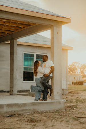 Interracial couple sharing romantic moment under porch of new home construction at golden sunset.