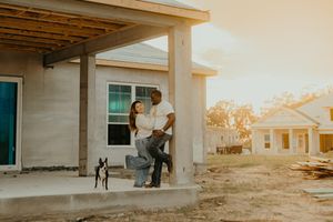 Interracial couple with Boston Terrier posing on porch of new construction home at golden hour sunset.