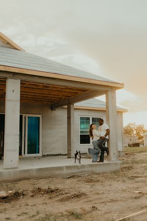 Couple standing on porch of new home under construction with small dog.