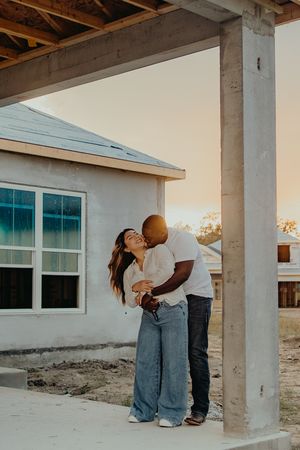 Couple sharing a tender kiss at golden hour outside their new home under construction.