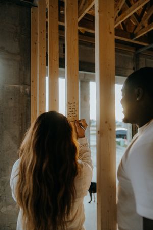 Woman writing on wooden beam stud inside home under construction.
